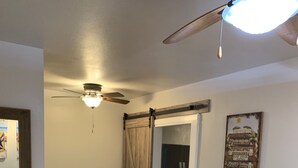 Ein Schlafzimmer mit Bett, Stuhl, Esstisch mit Stühlen, Deckenventilator und einem Bild an der Wand.