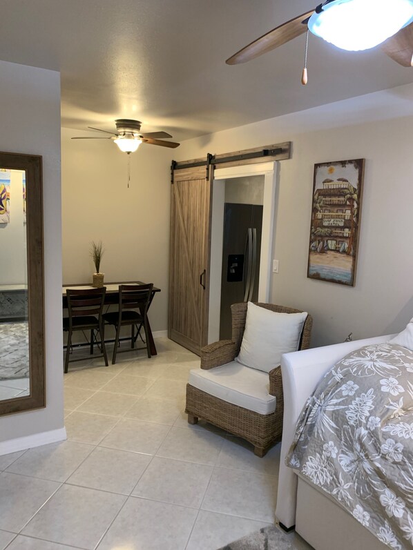 A bedroom with a bed, a chair, a dining table with chairs, a ceiling fan, and a painting on the wall. - Riverfront Luxury Hideaway (Sebastian)