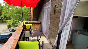 Une terrasse extérieure dotée d’une plateforme en bois, d’une table avec des chaises, d’un parasol rouge et d’une porte-fenêtre coulissante donnant sur un espace intérieur.
