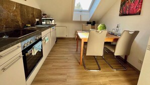 Une cuisine compacte équipée d’une cuisinière, d’un four à micro-ondes et de placards. On y trouve une table à manger avec des chaises et une petite fenêtre au-dessus.