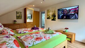 Une chambre avec deux lits, une commode en bois, un miroir et un téléviseur fixé au mur.