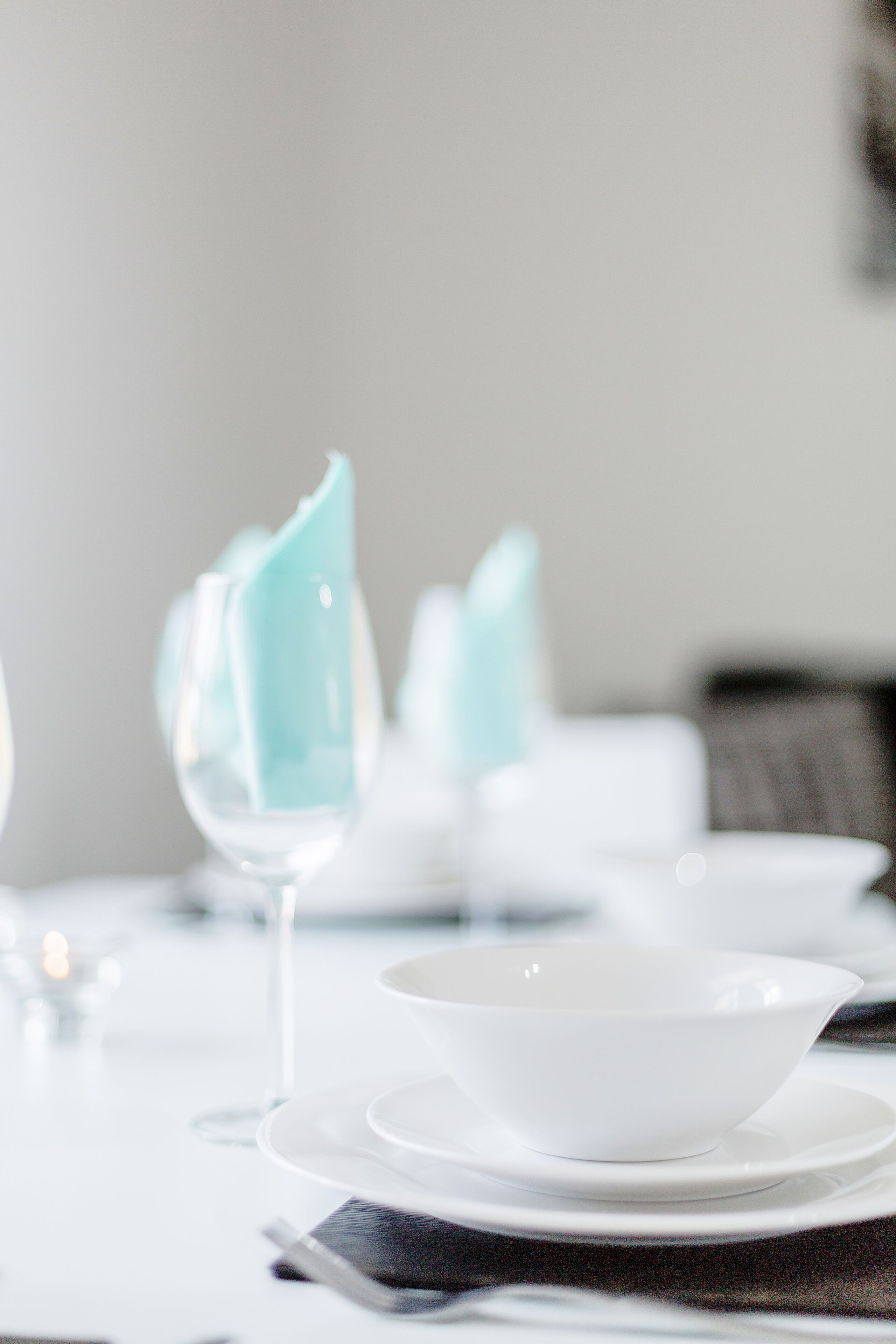 A dining table set with white plates, a clear glass, and a napkin holder with a blue napkin.
