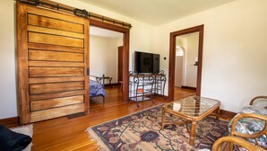 A room with a wooden sliding door, a glass-top table, a patterned rug, and a television in the background. - Residence on the Roundabout (St Charles)