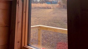 A wooden cabin with a large window, a hanging light fixture, and a view of a field with trees and a building in the distance. - Fun Treehouse Getaway • Firepit • Lake Access (Goreville)