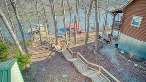 A cabin with a wooden deck, a covered area with a red roof, and a view of a lake. - Fun Treehouse Getaway • Firepit • Lake Access (Goreville)