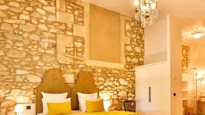 A bedroom with a stone wall, a bed with yellow bedding, a chandelier, and a white wardrobe. - Full of character, standing, SWIMMING POOL, large GARDEN, QUIET CHARM & BEAUTY (Avignon)