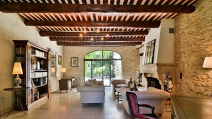 A spacious living room with a fireplace, a large window, and a stone wall. - Full of character, standing, SWIMMING POOL, large GARDEN, QUIET CHARM & BEAUTY (Avignon)