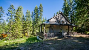 A cabin with a porch, surrounded by tall pine trees. - Luxe family and pet friendly chalet in private, forested setting (Leavenworth)