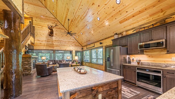 A spacious kitchen with a large island, wooden ceiling, and a stone fireplace.