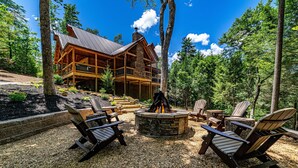 A lodge with a stone fireplace and Adirondack chairs in a forest setting.