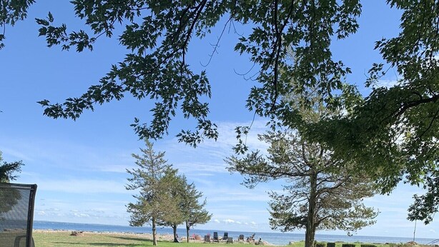 A wooden deck with a picnic table and chairs, overlooking a grassy area with trees and a view of the ocean. - Lake Ontario: Henderson, NY (Henderson)