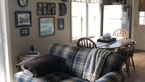 A living room with a plaid sofa, a dining table with chairs, a refrigerator, and a wall clock. - Lake Ontario: Henderson, NY (Henderson)