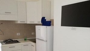 Cozinha compacta com armários brancos, geladeira branca e fogão a gás.