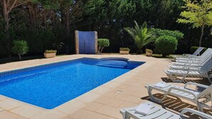 A rectangular swimming pool with a blue mosaic border, surrounded by beige tiles. There are white lounge chairs with towels on them, arranged in rows. - Villa V5 Piscine et Spa (São Bartolomeu de Messines)