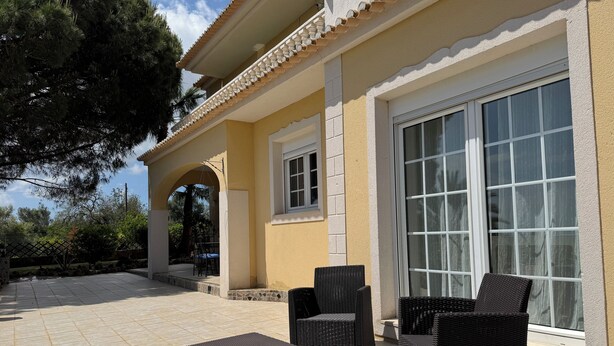A patio with wicker furniture and a large window. - Villa V5 Piscine et Spa (São Bartolomeu de Messines)