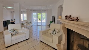 A spacious living room with two white sofas, a fireplace, and a dining area in the background. - Villa V5 Piscine et Spa (São Bartolomeu de Messines)