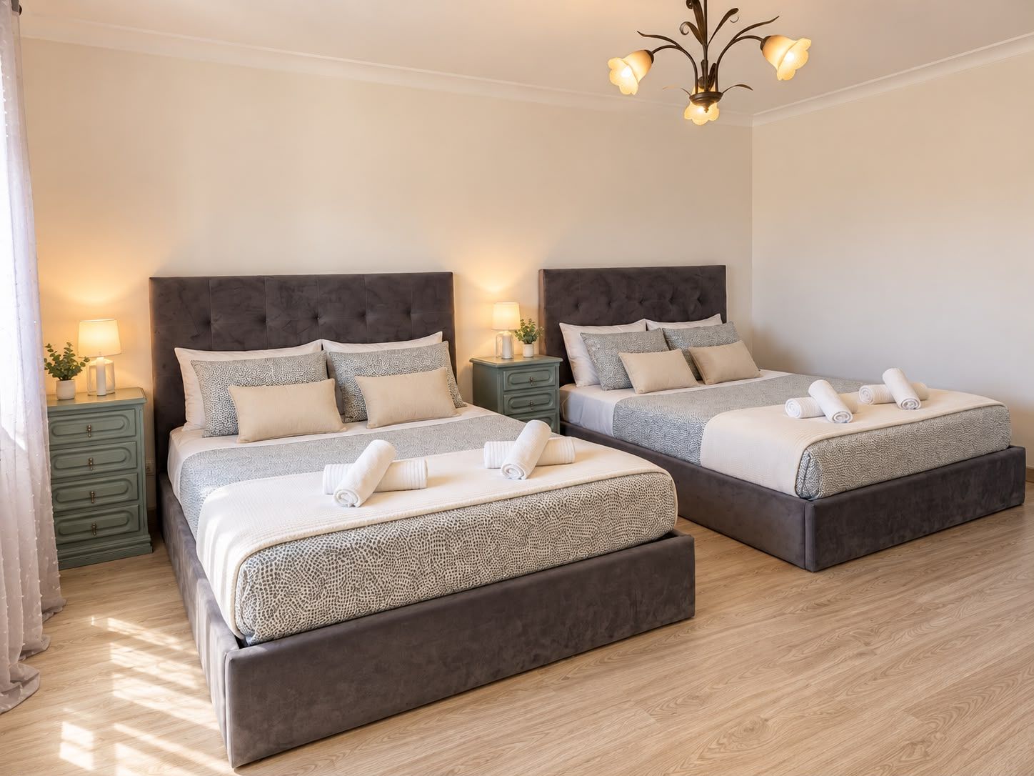 Een tweepersoonskamer met twee bedden, elk met een donkere hoofdbord, een nachtkastje met een lamp en een raam met gordijnen.