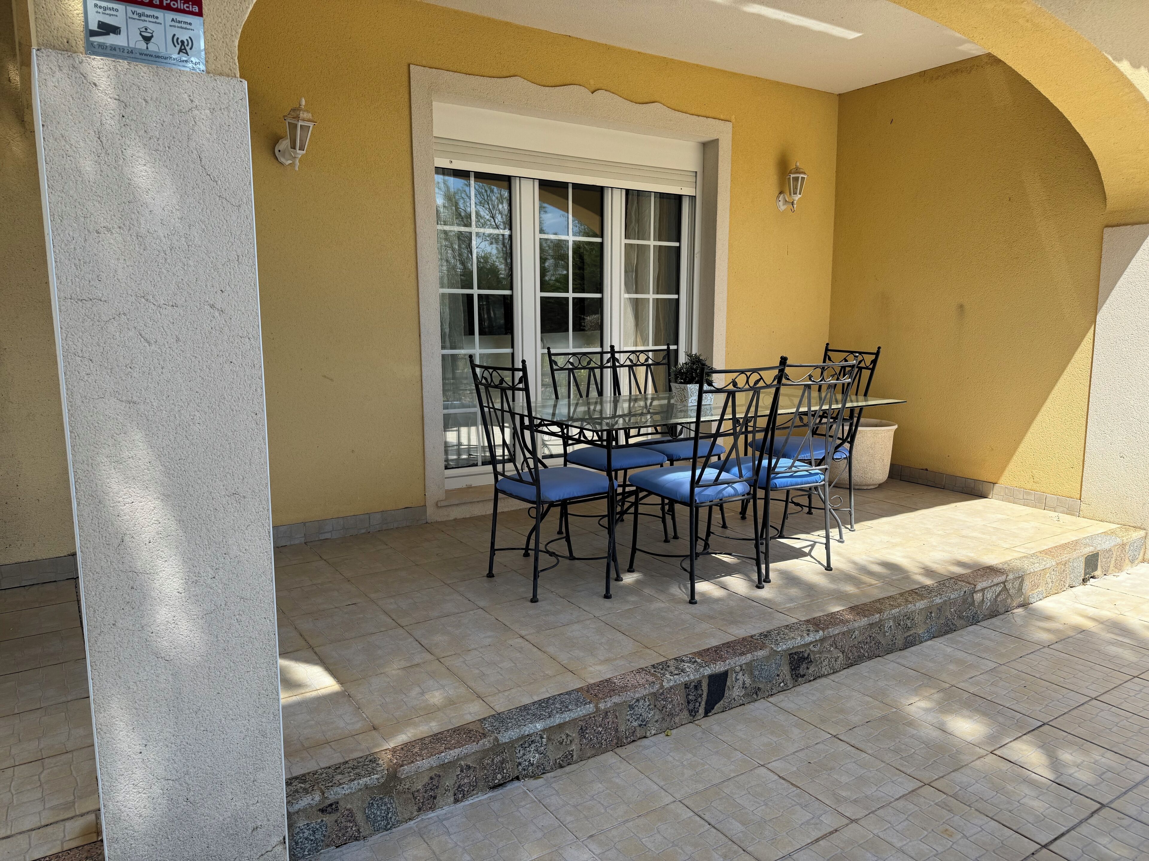 A patio with a table and chairs, a window, and a wall-mounted light fixture.