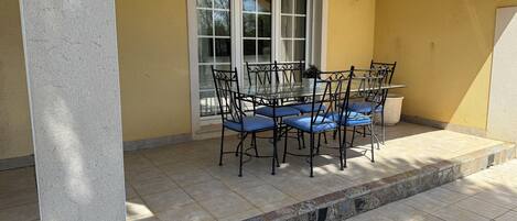 A patio with a table and chairs, a window, and a wall-mounted light fixture.