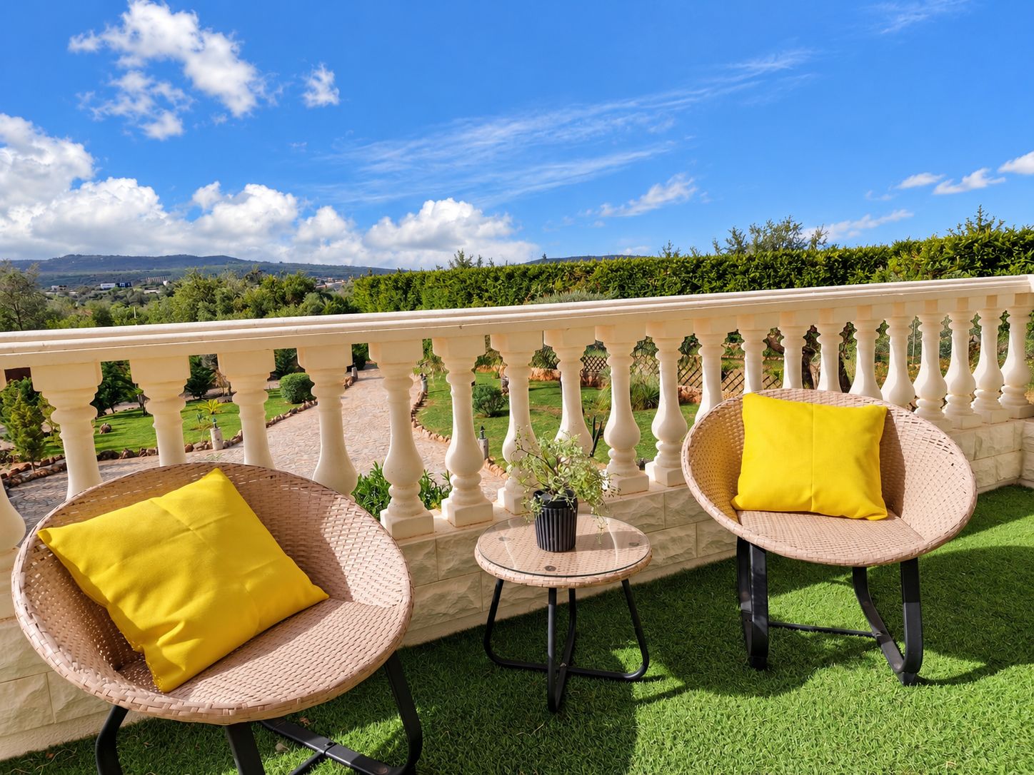 A balcony with wicker chairs and a small table, surrounded by a white balustrade.