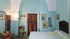 Een slaapkamer met een bed, een stoel, een houten garderobe en een wandplank.