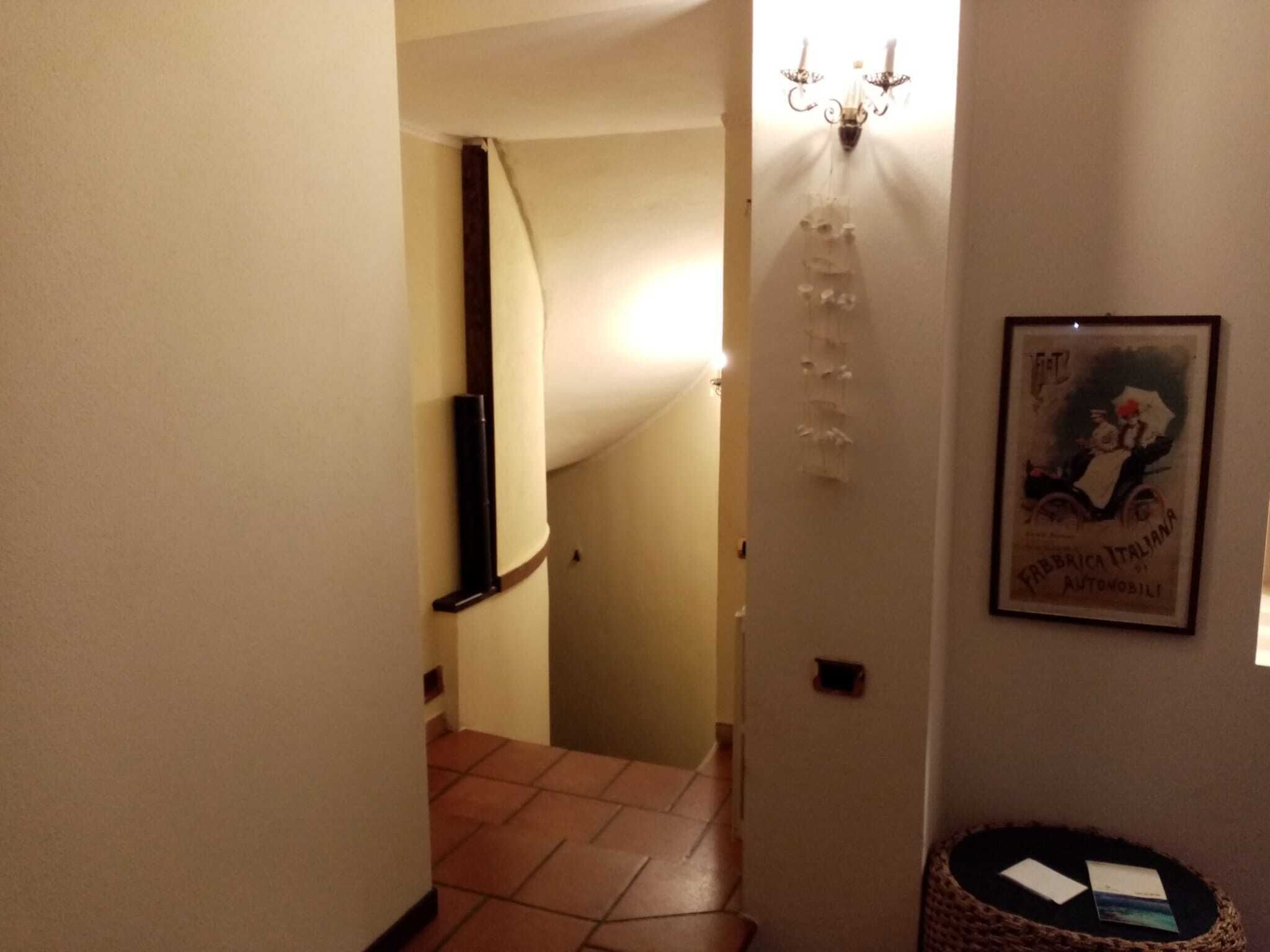 En smal hall med ett klinkergolv, en väggmonterad lampa och en inramad tavla.
