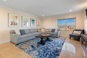 Uma sala de estar com sofá seccional, mesa de centro e uma janela grande com vista para a cidade.