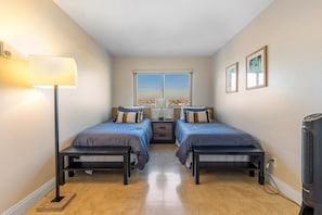 A room with two beds, a standing lamp, a window with a city view, and a heater. - Located right on the Balboa Peninsula, few steps from the beach and the harbor. (Newport Beach)