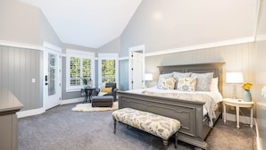 Quarto com cama grande, um banquinho, mesa de cabeceira e uma cadeira.