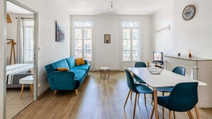 A modern living room with a blue sofa, a dining table with chairs, and large windows.