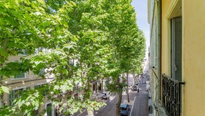 A narrow street lined with trees and buildings, featuring a parked car and a pedestrian.