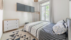 A bedroom with a bed, a dresser, a hanging light, and a window with curtains.