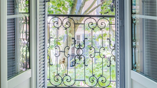 An open balcony with a metal railing, a view of a tree, and a building in the background.