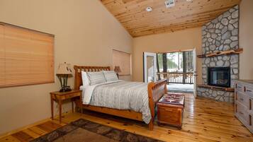A bedroom with a wooden bed, a stone fireplace, and a view of the outdoors.