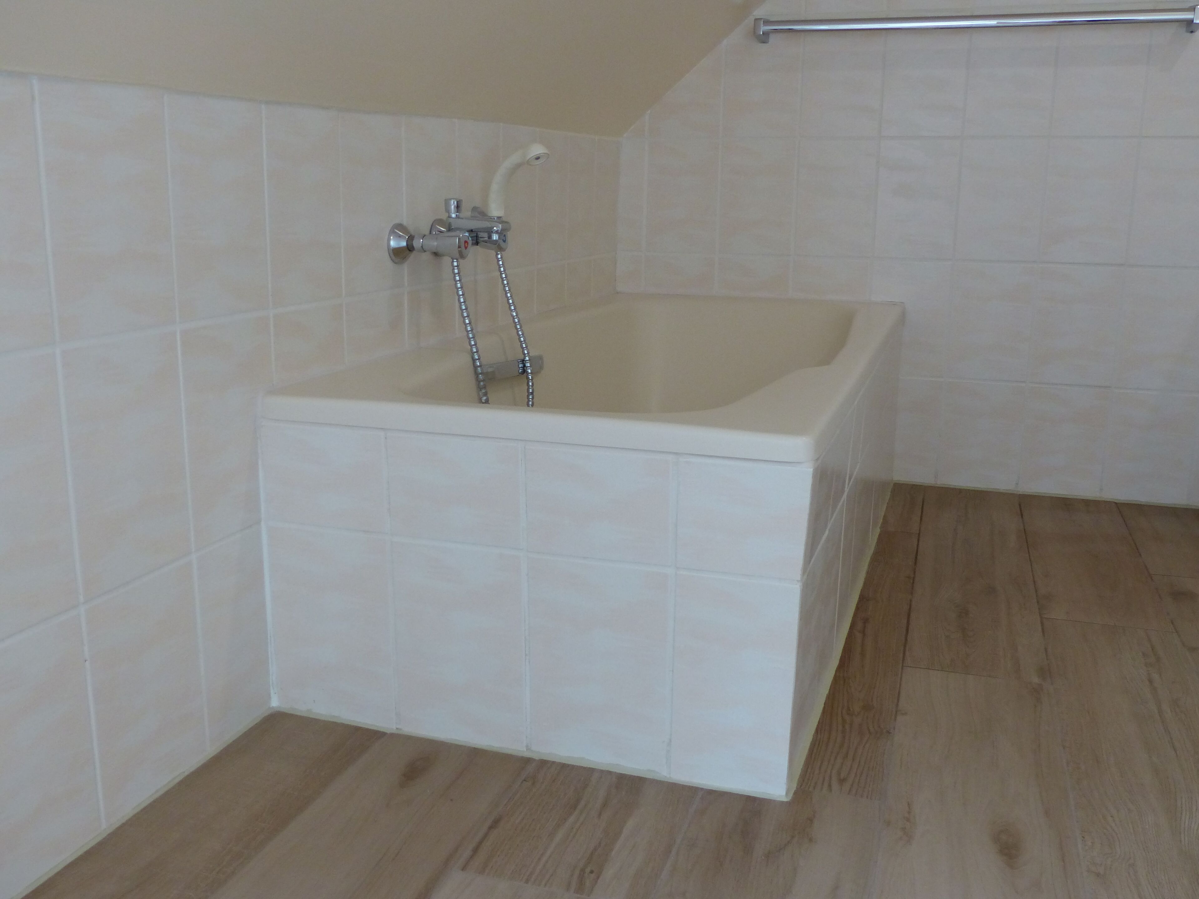 A bathroom with a white bathtub, tiled walls, and wooden flooring.