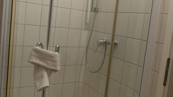 A glass-enclosed shower stall with white tiles, a handheld showerhead, and a towel rack with a white towel.