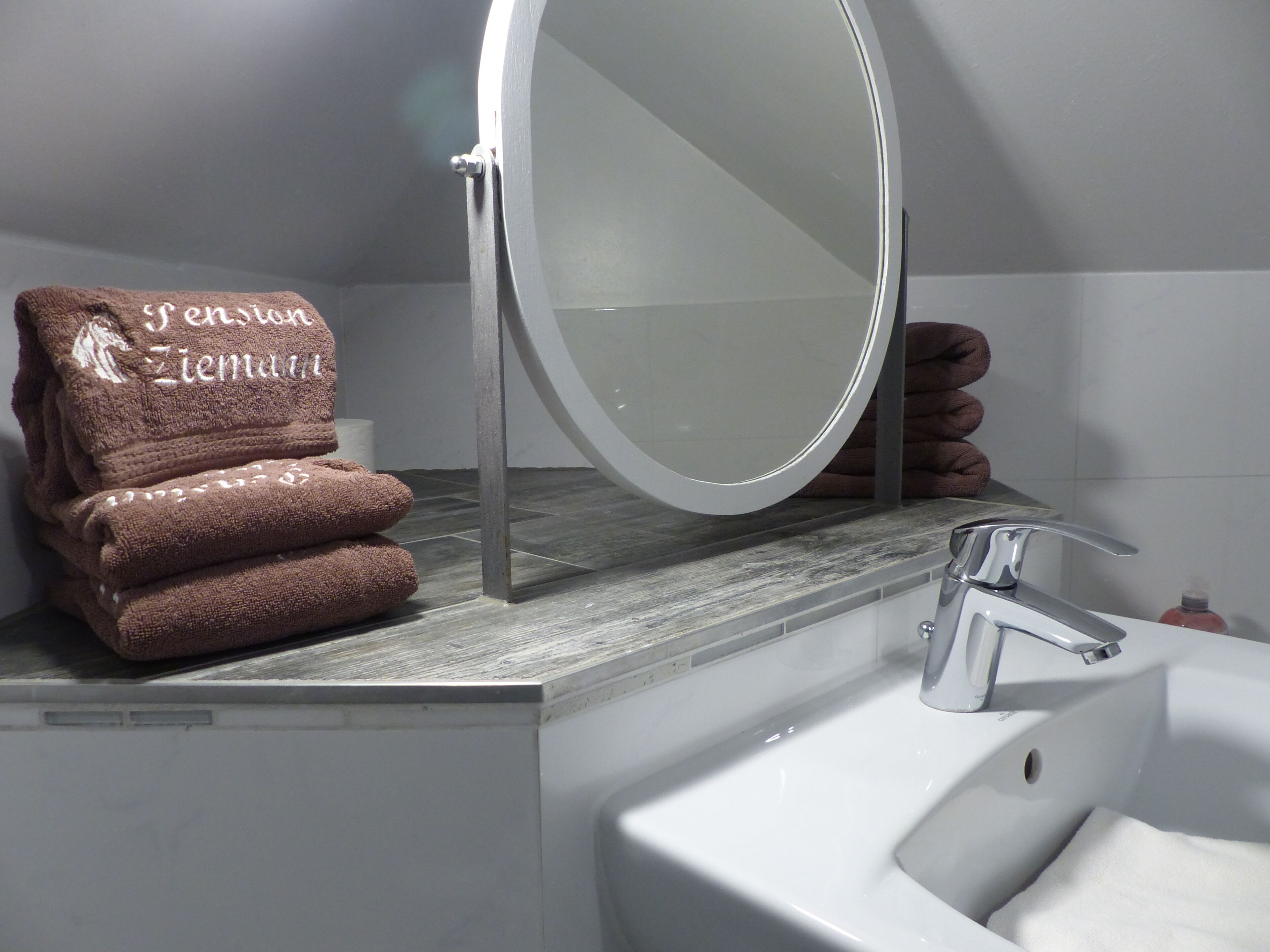 A bathroom with a sink, mirror, and stacked towels.