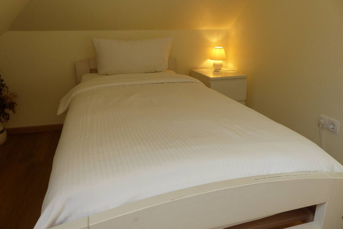 Ein ordentlich gemachtes Bett mit weißer Bettwäsche in einem Zimmer mit einem Nachttisch und einer Lampe.