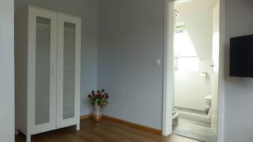 Een kamer met een houten vloer, een witte inloopkast en een deur naar een badkamer met toilet en douche.