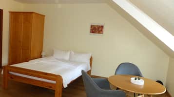 Une chambre avec un lit en bois, deux chaises grises, une petite table ronde ornée d’une plante et une armoire en bois.