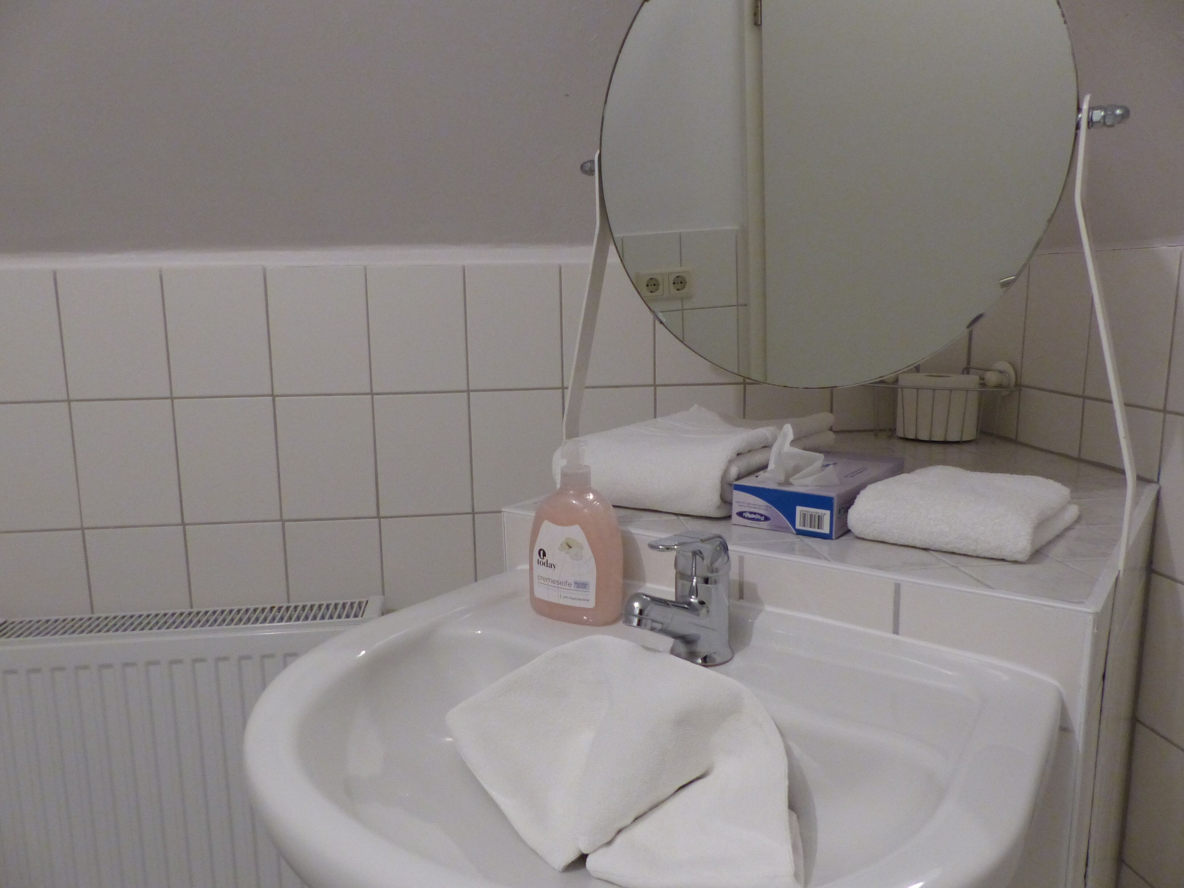 Un baño con un lavamanos blanco, un espejo y un perchero para toallas.