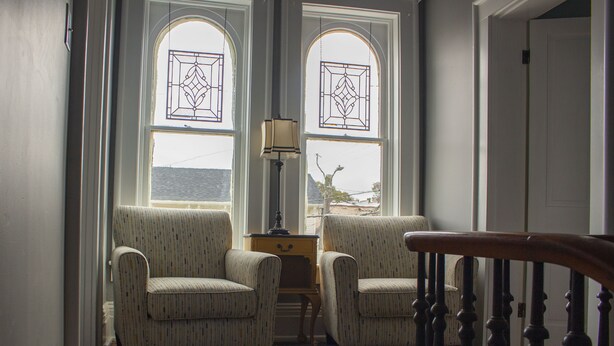 A room with two upholstered chairs, a small table with a lamp, and a view through a window with a decorative glass design. - Artistic Lodging Queen suite (Paris)