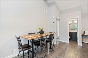 A dining area with a wooden table and black chairs, a potted plant, and a view into a kitchen area.