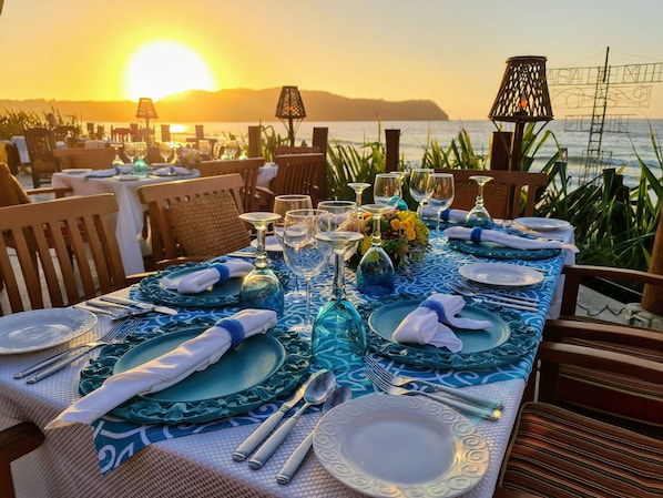 A table set for dinner with a view of the sunset over the water.