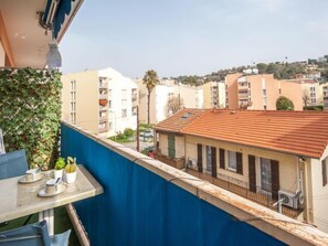 A balcony with a view of residential buildings, a table with cups and a plant, and a blue curtain. - L'Amiral by Interhome (Cagnes-sur-Mer)