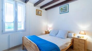 Cozy retreat with a single bed, nightstand, and bedside table, featuring two windows with white curtains and framed pictures on the wall.
