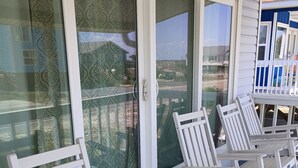 Un porche cubierto con mecedoras blancas y un ventanal con cortinas decorativas.