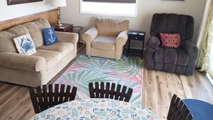 Una sala de estar con sofá, sillón y una mesita de noche con lámpara.