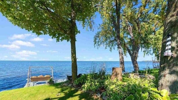 A serene lakeside garden with a swing, lush greenery, and a clear view of the water. - WATERFRONT DOOR COUNTY HOME.  Gorgeous Sunsets. 3 Bedrooms. Sleeps 6.   5 star! (Door County)