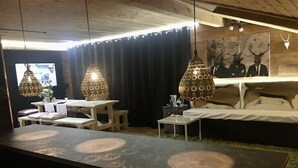 Una habitación con una larga mesa, dos lámparas colgantes, una cama, un cuadro y un televisor.